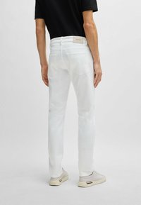 Jeans in denim bianco a vestibilità slim, design a cinque tasche e patch con logo sulla vita posteriore. Texture liscia con dettagli di cucitura minimi.