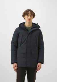 Dark blue padded parka jacket with a hood, featuring two front pockets and a zip closure, designed for warmth and protection.
