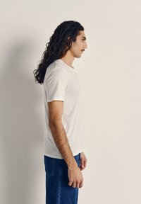 Bela bombažna majica z okroglim izrezom, kratkimi rokavi in sproščenim krojem, kombinirana s sivkami modre jeans hlače. Gladek tekstura, minimalen dizajn.