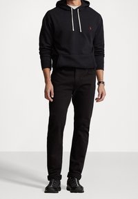 Svart hoodie med snörning, logotyp på bröstet, kombinerad med mörka byxor och svarta sneakers. Avslappnad passform och enfärgade.