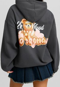 Sudadera gris de gran tamaño con un gráfico colorido de un oso y el texto juguetón "2k Mood No Drama" en la parte posterior, con una textura suave y lisa.