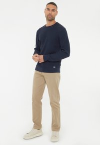 Marinefarbener strukturierter Strickpullover mit langen Ärmeln, kombiniert mit hellbeigen Chinos und weißen Sneakers. Schlichtes Design mit gerippten Bündchen und Saum.
