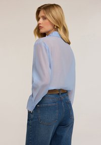 Blusa leggera blu chiaro con maniche lunghe, polsini abbottonati e colletto, abbinata a jeans in denim a lavaggio medio con tasche posteriori.