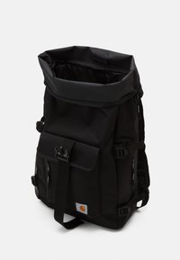 Sac à dos noir à rouleau fabriqué en matériau durable, avec des sangles réglables, plusieurs poches et un patch de logo bien visible.