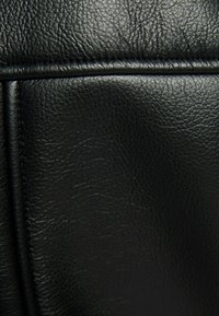 Svart texturerat lädermaterial som visar en närbild, vilket framhäver fina kornmönster och släta sömnadsdetaljer.