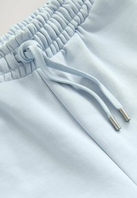 Pantalones de chándal azul claro con cintura fruncida, cordón con puntas de metal y suave tela de mezcla de algodón. Textura suave en toda la prenda.