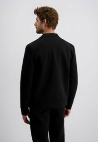Schwarzer Sweatshirt mit hohem Kragen, glatter Textur und gerippten Bündchen. Verfügt über eine Nahtdetail auf der Rückseite und ein Akzent auf dem linken Ärmel.