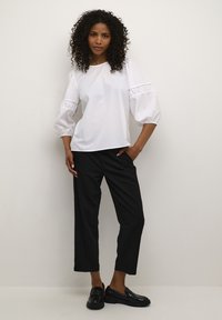 Hvid, langærmet bluse med samlede puffærmer; sat sammen med sorte, lige bukser og glossy sorte loafers. Minimalistisk design.