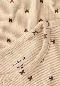 Beżowa koszulka z prążkowanej tkaniny z małymi brązowymi wzorami motyli, okrągłym dekoltem i metką z nazwą marki "name it."