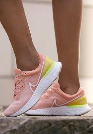 Personne portant des chaussures de course Nike roses et jaunes marchant sur un pavé en pierre à l'extérieur.