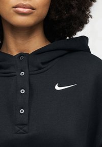 Schwarzes Kapuzensweatshirt mit geknöpfter Blende, weichem Stoff und weißem Nike-Logo auf der Brust; ausgestattet mit schwarzen Knöpfen und einer strukturierten Kapuze.