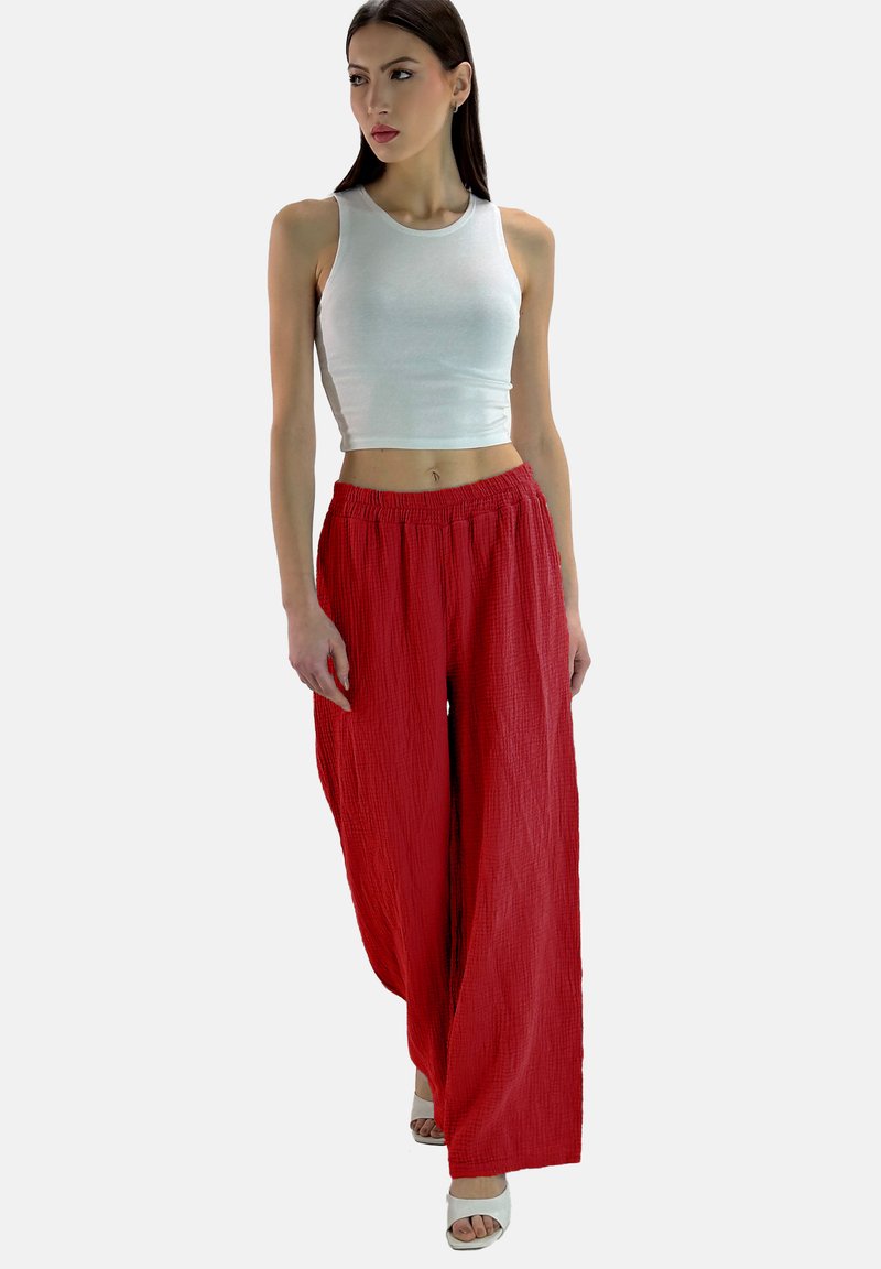 Pantaloni rossi a gamba larga e stropicciati con vita elastica, abbinati a un top corto senza maniche bianco e a tacchi aperti bianchi.