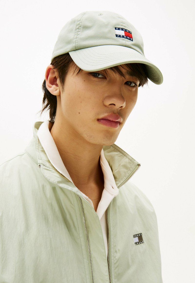 Gorra de béisbol verde claro con parche de logo; cortavientos a juego verde claro con cremallera; cuello blanco visible. Tejido suave, diseño casual.