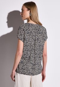 Halenka s krátkým rukávem v vlnitém černobílém vzoru, s kulatým výstřihem a detailem zadní sklady pro pohodlné nošení.