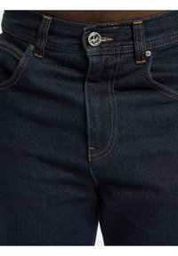 Denim jeans v temno modri barvi, z gumbom namesto zadrge, rumenim šivom in klasično zasnovo s petimi žepi. Gladka tekstura, trdna konstrukcija.