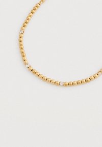 Χρυσό βραχιόλι με πεταλίδες καστανών και ομοιόμορφα τοποθετημένα μικρά διαυγή πετράδια σε ελαφρύ ουδέτερο φόντο.