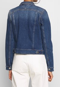 Dark blue denim jacket, fitted design, classic collar, subtle stitching details, metal hardware accents, cropped length at the waist.