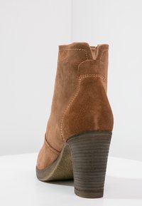 Bruine suède enkellaars met een gestapelde hak, ronde neus en zichtbare stiksels. Gladde textuur met een lichte glans op de hak.