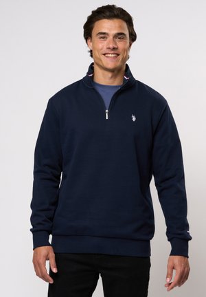Marineblå hettegenser med glidelås i kragen, ribbede mansjetter og nederkant, som har et lite brodert logo på brystet og et strukturert, mykt stoff.