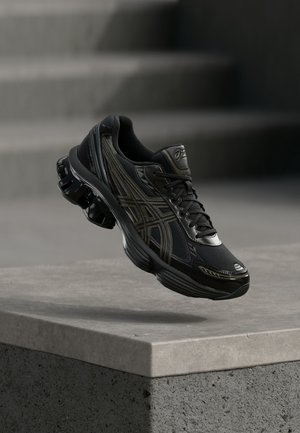 Zwarte sportsneakers met dikke zool en tussenzool met luchtkussen, zwevend boven een betonnen rand met wazige treden op de achtergrond.