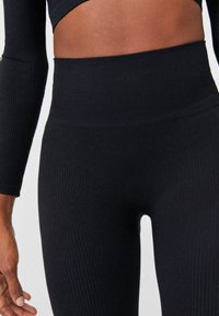 Zwarte geribbelde leggings met een hoge taille, voorzien van een gladde tailleband en een strakke pasvorm, die de textuur van de stof en de lichaamsvorm benadrukken.