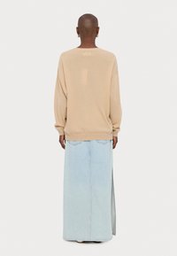 Beżowy, oversize'owy sweter z opuszczonymi ramionami, w połączeniu z jasnoniebieską, długą spódnicą z denimu, posiadającą boczny rozcięcie i dwie tylne kieszenie.