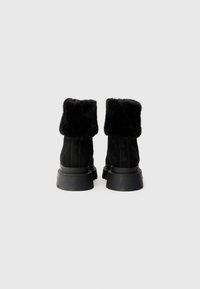 Bottes en daim noir avec un col en fourrure noire, présentant une semelle en caoutchouc noir épaisse et des détails de couture verticale.