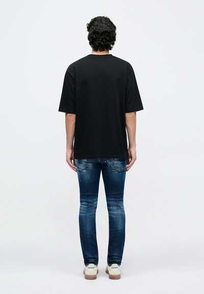 Black short-sleeve t-shirt with a relaxed fit, paired with dark blue jeans featuring a light wash. The outfit is completed with white sneakers.