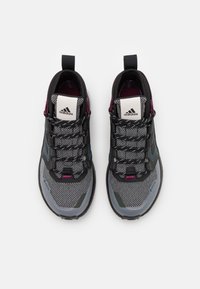 Chaussures de sport noires et grises avec tissu en maille, accents violets et semelle texturée. Présentent un design à lacets et un logo sur la languette.