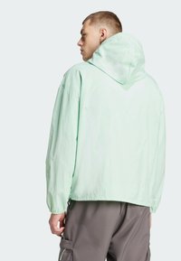 Miętowa zielona kurtka z kapturem, wykonana z lekkiego materiału, charakteryzująca się luźnym krojem, opadającymi ramionami i elastycznymi mankietami.