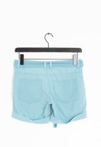 Shorts en coton bleu clair avec revers, dotés de deux poches à l'arrière et d'une passants de ceinture à la taille, suspendus à un cintre noir à pince.