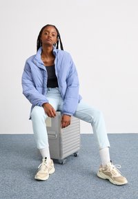 Puff jacket in light blue fabric with a high collar, paired with fitted black top and light blue jeans. Beige sneakers with textured accents.