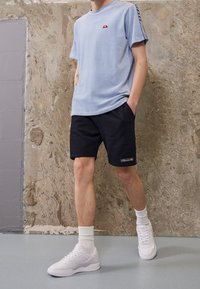 T-shirt bleu clair côtelé avec petit logo, short noir, baskets blanches et chaussettes blanches. Tissu lisse, coupe décontractée et style casual.