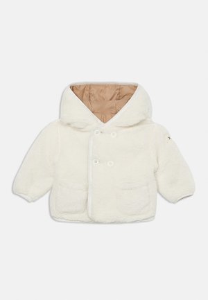 Veste blanche duveteuse avec une grande capuche, à double boutonnage à l'avant et deux poches à l'avant ; doublée de matériau beige, avec des boutons ronds.