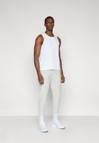 Λευκό αμάνικο τοπ συνδυασμένο με ανοιχτό γκρι παντελόνι με στενή εφαρμογή. Το μοντέλο φορεί λευκά αθλητικά παπούτσια και καλτσάκια μέχρι τον αστράγαλο. Απλός σχεδιασμός, αεριζόμενο ύφασμα.