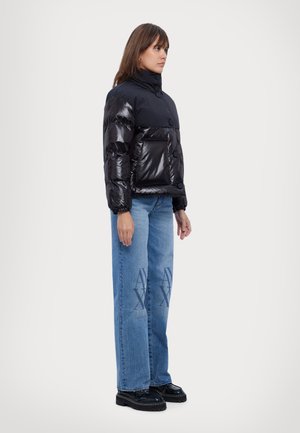 Doudoune noire avec une texture brillante, col haut et boutons. Assortie avec un jean bleu surdimensionné présentant un détail de logo à l'avant.