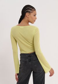 Gul langermet tettsittende topp med rund hals, matchet med høyt midje svarte jeans med baklommer og en cropped design.