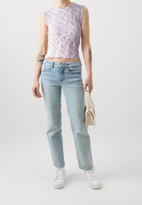Fialový texturovaný crop top s vlnitými okraji, zkombinovaný se světle modrými rovnými džínami a bílými teniskami. Drží krémovou tašku.