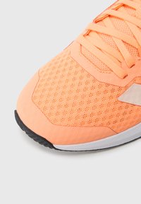 Pomarańczowy but sportowy z cholewką z siateczkowego materiału, płaskimi sznurowadłami i gumową podeszwą zapewniającą przyczepność. Charakteryzuje się lekką konstrukcją i gładkim wykończeniem.