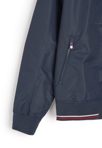 Granatowa, lekka kurtka z zamkiem błyskawicznym, z kieszenią zapinaną na suwak, ściągaczami na rękawach oraz paskiem w czerwono-biało-niebieskie paski. Gładka faktura, nowoczesny krój.