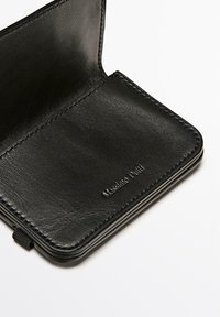Sort læderpung med en glat overflade, der har et simpelt, foldbart design og prægede mærke navn på indersiden.
