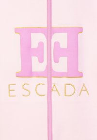 Tessuto rosa con grande logo "EE" rosa contornato d'oro sopra il testo "ESCADA" ricamato in oro e una cucitura verticale centrale.