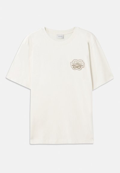 Krēmkrāsas T-krekls ar īsām piedurknēm, izgatavots no mīksta kokvilnas. Iezīmēts ar apļveida izšūtu logotipu kreisajā krūtī bēšo toņu krāsā. Kvadrātveida forma.