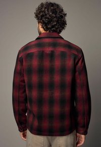 Chemise en flanelle à carreaux rouge et noir, avec un col, des poignets à boutons et un tissu légèrement texturé, conçue avec une coupe décontractée.