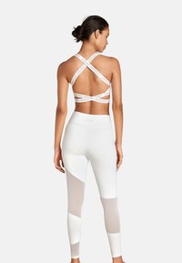 Weißes Sportoutfit bestehend aus einem Bralette mit Kreuzträgern und Logo, sowie high-waisted Leggings mit matten und Mesh-Panel-Details.