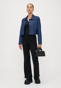 Jeansjakke i mørkeblått med en cropped design, fire knapper og krage; sammen med en svart blondetopp og vide svarte bukser.