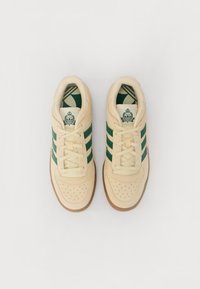 Beige semskinn-sportssko med grønne striper og perforert tådetalj. Gummisåle i gummi og mønstrete innersåle. Snører og polstret krage inkludert.