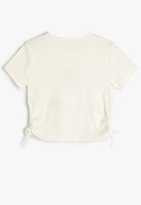 Top corto de manga corta blanco con cuello redondeado y lados fruncidos que cuentan con lazos ajustables para personalizar el ajuste.