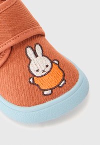 Dětská obuv v rezavé barvě s světle modrou podešví a výšivkou bílé králíka v oranžovém oblečku na špičce.
