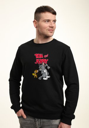 Sort sweatshirt med en grafisk print af Tom og Jerry. Nøglefunktioner inkluderer levende farver og tegneseriestil karakterer. Fabrik af bomuldsblanding.